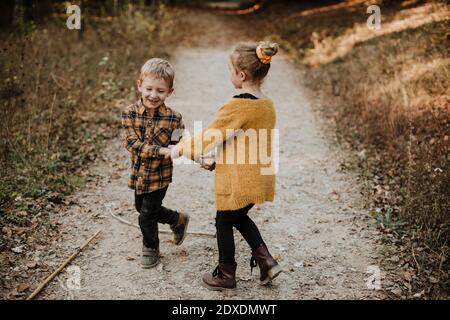 Lächelndes Mädchen und Bruder halten sich die Hände beim Spielen im Wald Stockfoto