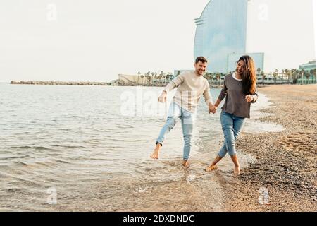 Glückliches junges Paar, das Spaß hat, während man am Strand gegen läuft Der Himmel ist klar Stockfoto