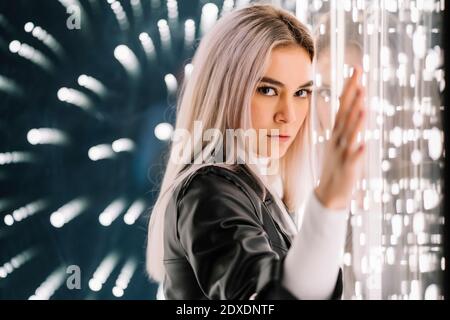 Attraktive Frau, die sich an einer beleuchteten Glaswand lehnt Stockfoto