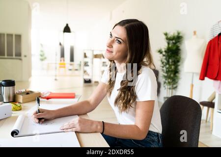 Nachdenklich weibliche kreative Designerin Zeichnung im Buch, während sitzen studio Stockfoto