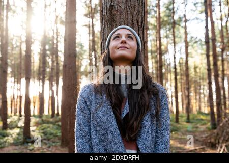 Nachdenkliche Frau, die aufschaut, während sie gegen den Baumstamm steht Cannock Chase Forest Stockfoto