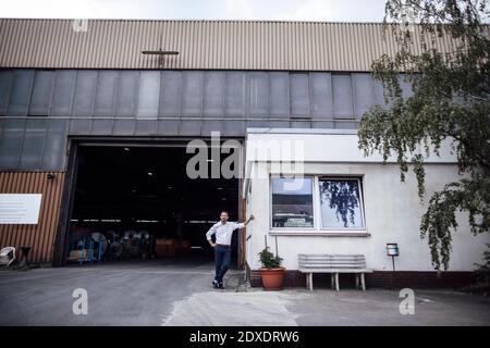 Männlicher Unternehmer, der sich auf die Kabine stützt, während er gegen den Eingang der Fabrik steht Stockfoto