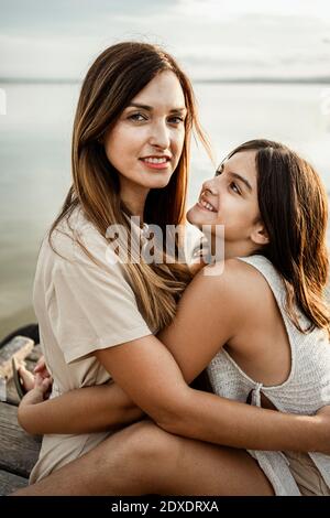 Mutter und Tochter umarmen sich am Steg am See Stockfoto