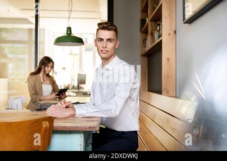 Junger Geschäftsmann sitzt auf dem Tisch mit Kollegen im Hintergrund arbeiten Im Büro Stockfoto