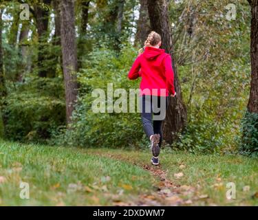 Junge Sportlerin beim Joggen auf Gras im Wald Stockfoto