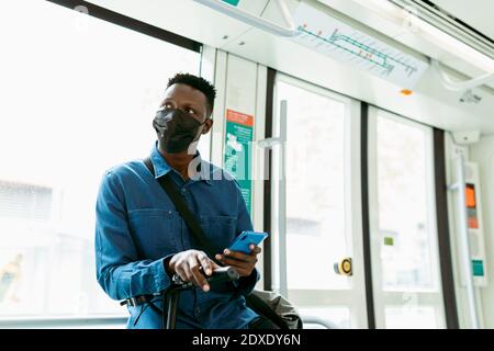 Afrikanischer Geschäftsmann trägt eine schützende Gesichtsmaske während der Reise durch den Zug Stockfoto