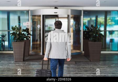 Geschäftsmann zieht Gepäck mit Rädern, während er das Hotel verlässt Stockfoto