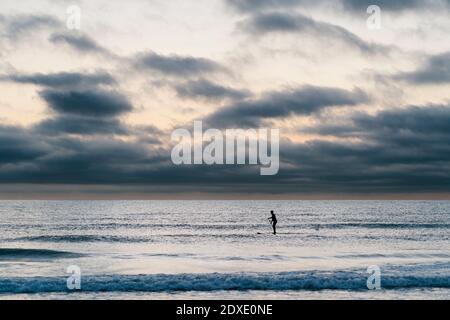 Weibliche Paddlebarderin beim Surfen im Meer während der Dämmerung Stockfoto