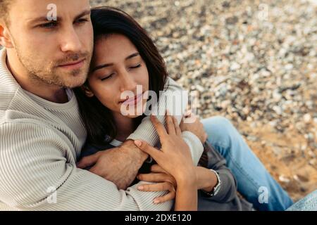 Junger Mann umarmt Frau beim Blick weg auf den Strand Stockfoto