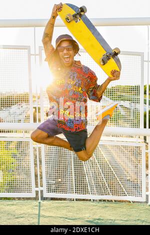 Fröhlicher Mann mit Skateboard springen auf Brücke Stockfoto