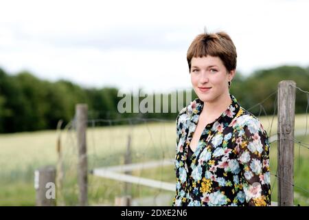 Junge Frau trägt Blumenkleid steht gegen Zaun Stockfoto