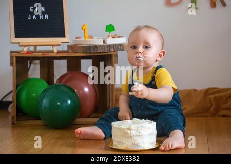 Niedlichen Baby Junge essen Kuchen, während auf dem Boden sitzen Zu Hause Stockfoto