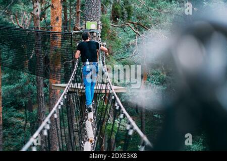 Junger Mann überquert Seilbrücke im Abenteuerpark Stockfoto