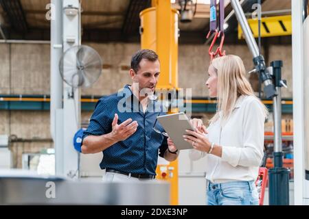 Geschäftsmann und Kollegin diskutieren während der Verwendung von digitalen Tablet stehen In der Industrie Stockfoto