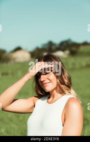 Junge Frau, die ihre Augen mit der Hand im Park während abschirmt Sommer Stockfoto