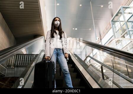Frau mit Gesichtsmaske, während sie mit Gepäck auf der Rolltreppe steht An der U-Bahn-Station Stockfoto