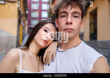 Junge Frau, die sich auf die Schulter des Mannes lehnt, während sie gegen das Gebäude steht Stockfoto
