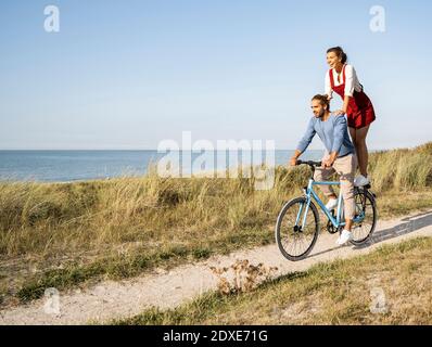 Junge Frau genießt Fahrt mit dem Mann, während auf dem Fahrrad stehen Gegen klaren Himmel Stockfoto