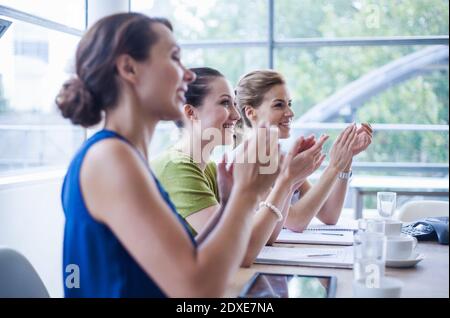 Glückliche weibliche Kollegen applaudieren, während im Vorstandszimmer sitzen während Meeting im Büro Stockfoto