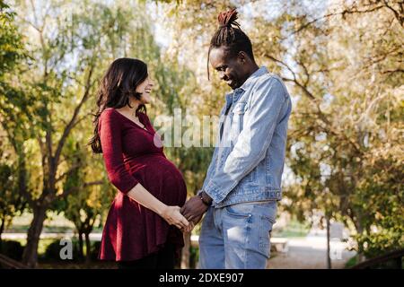 Glücklicher Mann, der den Magen einer schwangeren Frau im Park ansieht Stockfoto