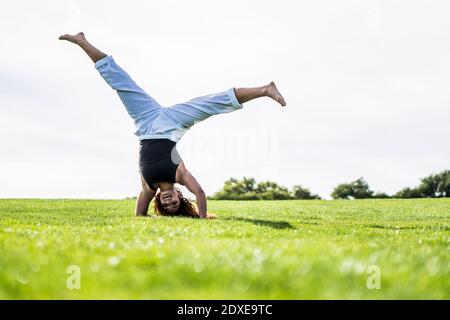 Sportlerin beim Handstand auf Gras im Park gegen klaren Himmel Stockfoto