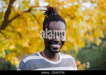 Lächelnder junger Mann, der während der Zeit gegen einen gelben Baum im Park steht Herbst Stockfoto