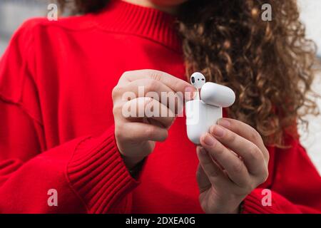 Junge Frau in rotem Pullover, die kabellose in-Ear-Kopfhörer entfernt Stockfoto