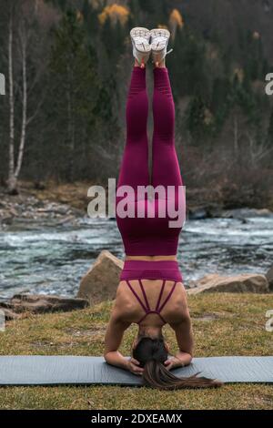 Aktive junge Frau, die Kopfstand auf einer Yogamatte im Ordesa Nationalpark, Huesca, Spanien praktiziert Stockfoto