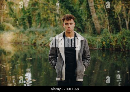 Junger Mann mit Händen in Taschen, die gegen den See stehen Stockfoto