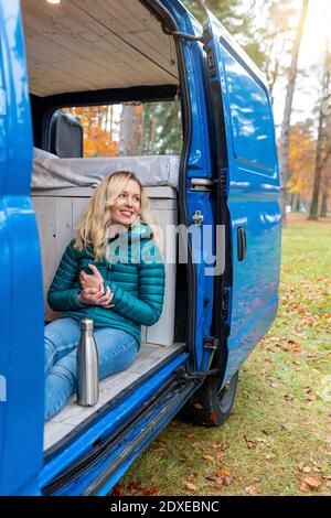 Glückliche Frau, die wegschaute, während sie die Teetasse an der Tür hielt Des Wohnwagens Stockfoto