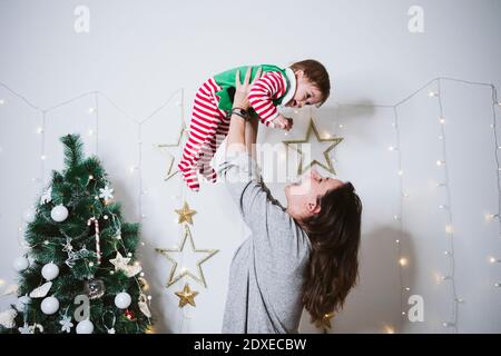 Lächelnde Frau Abholung Baby Junge während zu Hause spielen Zu Weihnachten Stockfoto