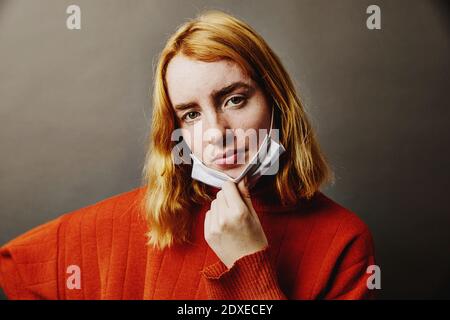 Teenage-Mädchen trägt Schutzmaske unter Kinn während des Stehens Vor grauem Hintergrund Stockfoto