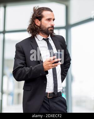 Porträt eines bärtigen Geschäftsmannes, der drinnen mit einem Smartphone steht Hand Stockfoto