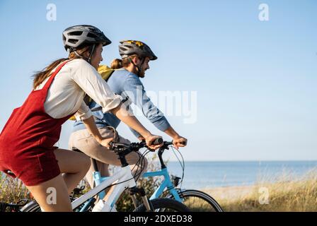 Junge Freundin und Freund fahren Fahrräder gegen klaren Himmel Stockfoto