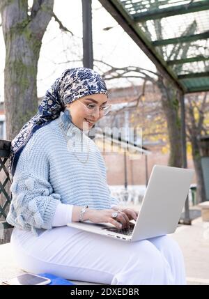 Junge Frau lächelt während der Arbeit auf Laptop im Freien Stockfoto