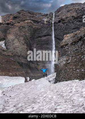 Männlicher Forscher, der auf Felsen gegen Wasserfall in Langjokull, Island, steht Stockfoto