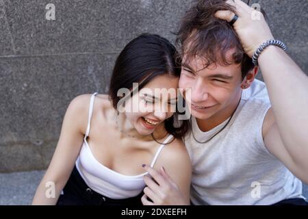 Fröhliches junges Paar, das an der Wand sitzt Stockfoto