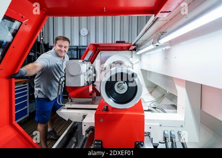 Lächelnder männlicher Arbeiter, der bei Maschinen in der Industrie steht Stockfoto