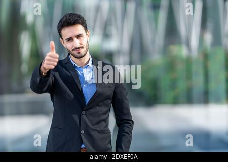 Junger Geschäftsmann im Anzug mit Daumen nach oben, während er im Freien steht Stockfoto