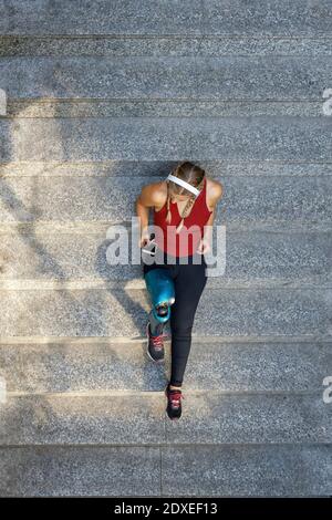 Junge Amputierte tragen Kopfhörer mit Handy, während sie sitzen Schritte Stockfoto