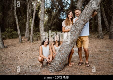 Eltern mit Töchtern, die hinter Baumstamm im Wald stehen Stockfoto