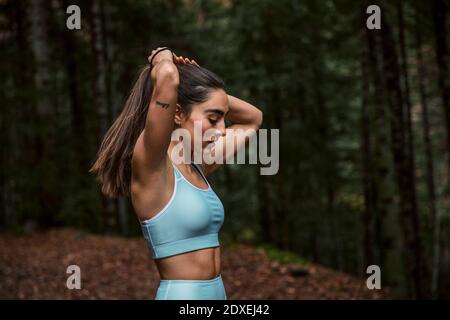 Frau, die Pferdeschwanz macht, während sie im Wald steht Stockfoto