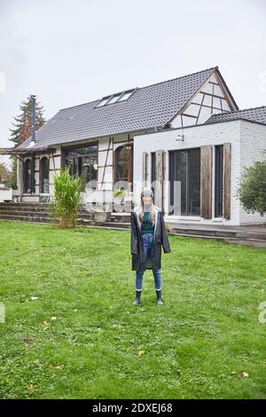 Reife Frau trägt Regenmantel stehen im Hinterhof gegen Haus Stockfoto