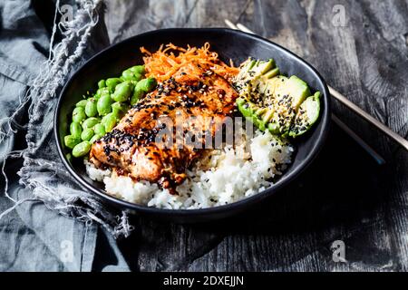 Schüssel Teriyaki Lachs mit Reis, Karottensalat, Edamame-Bohnen, Avocado und Sesam Stockfoto