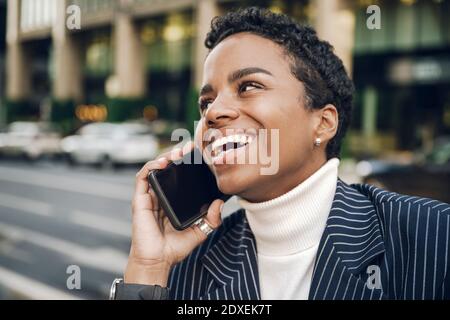 Glückliche junge Geschäftsfrau, die wegschaut, während sie auf dem Smartphone spricht Stockfoto