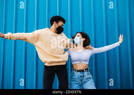 Sorgloses Paar trägt Gesichtsmaske tanzen, während sie gegen blau stehen Wand Stockfoto