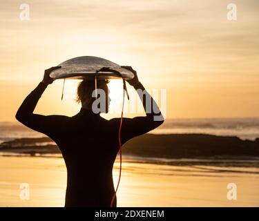 Silhouette Surfer trägt Surfbrett über Kopf am Strand während Sonnenuntergang Stockfoto