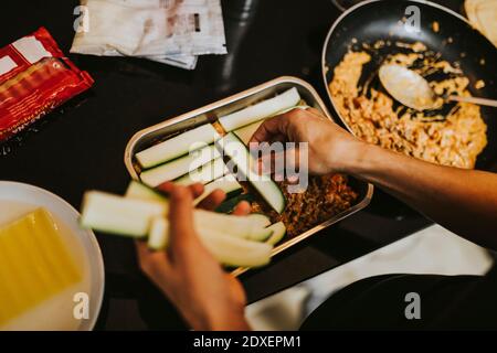 Frau, die im Stehen gehackte Zucchini in Lasagne-Kochplatte arrangiert In der Küche Stockfoto