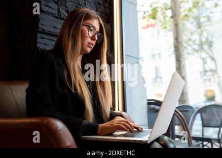 Junge Frau trägt eine Brille mit Laptop, während sie im Café sitzt Stockfoto