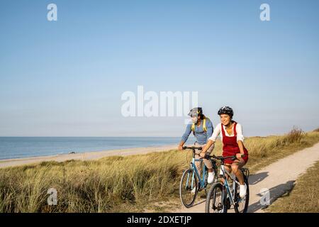 Lächelnde Frau trägt Fahrradhelm Fahrrad fahren mit Mann gegen Der Himmel ist klar Stockfoto